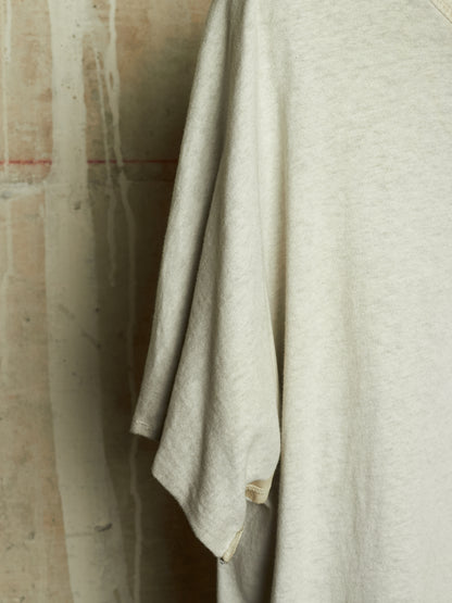 A close-up of a light heather gray or off-white t-shirt hanging against a textured concrete wall.