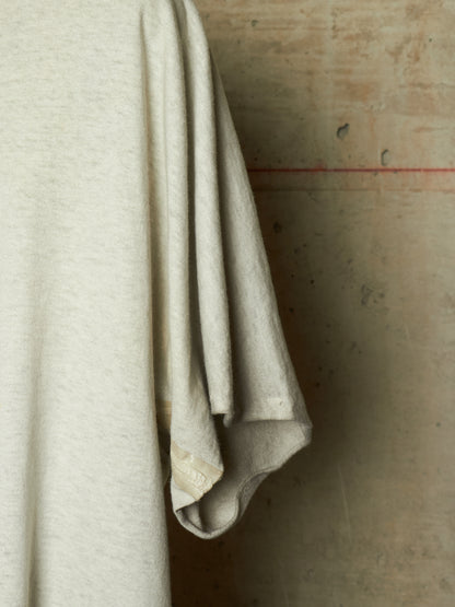 A close-up of a light beige or off-white knit fabric draped vertically against a textured concrete wall.