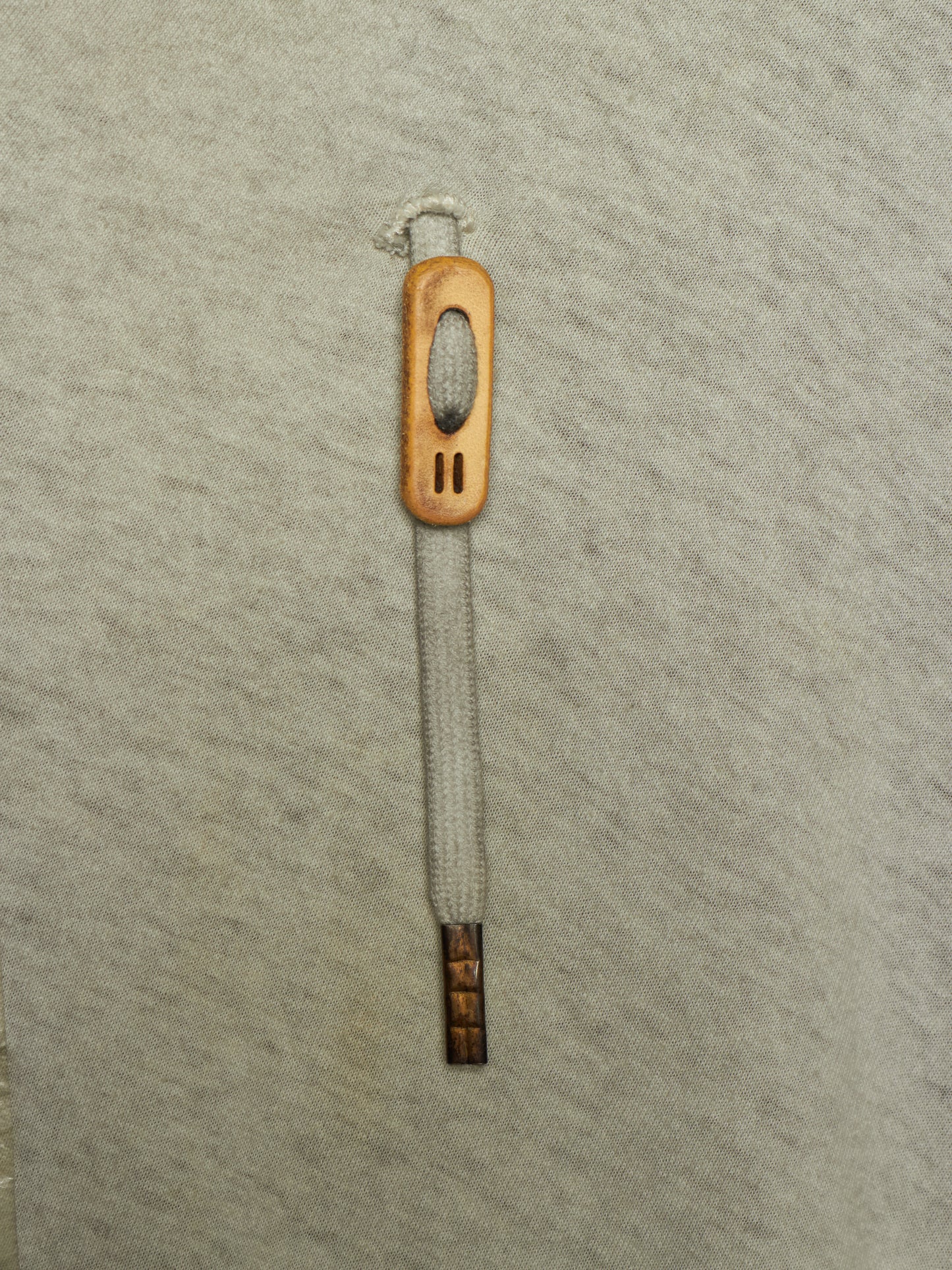 A single wooden shoe pull tab with a light gray woven rope handle, shown vertically on a textured light gray background.