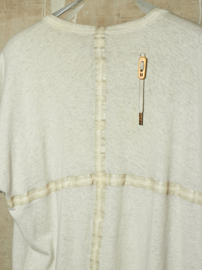 A close-up of the back of a cream-colored knit sweater with a unique vertical seam detail and a decorative gold-toned tag attached near the upper back.