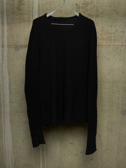 A black long-sleeve knit top hanging on a metal hanger against a textured concrete wall.