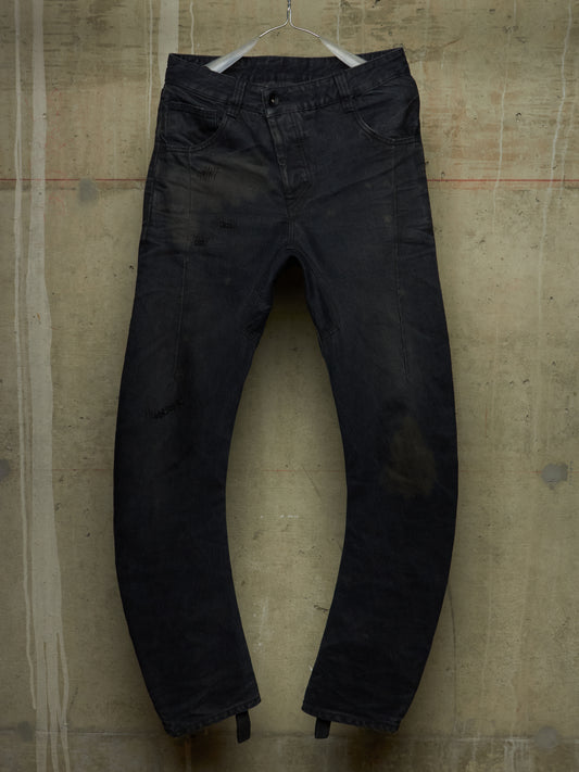 A pair of faded black denim jeans hanging on a white plastic hanger against a textured concrete wall.