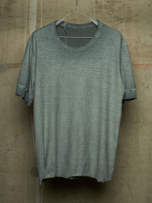 A short-sleeve crewneck t-shirt in heather gray, hanging on a wire hanger against a textured concrete wall.