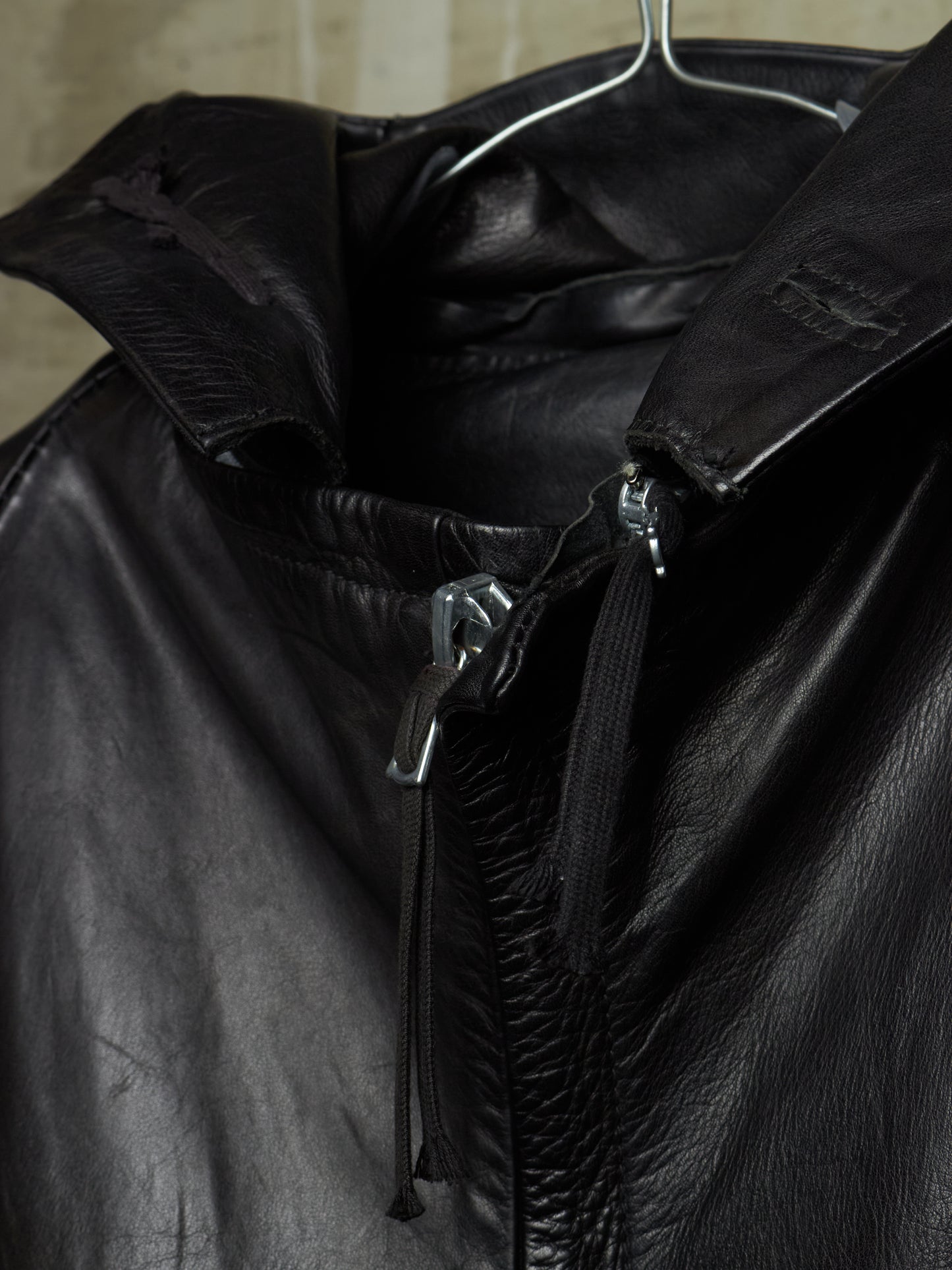 Close-up of a black leather jacket with a high collar and silver-toned zipper hardware, hanging on a metal hanger.