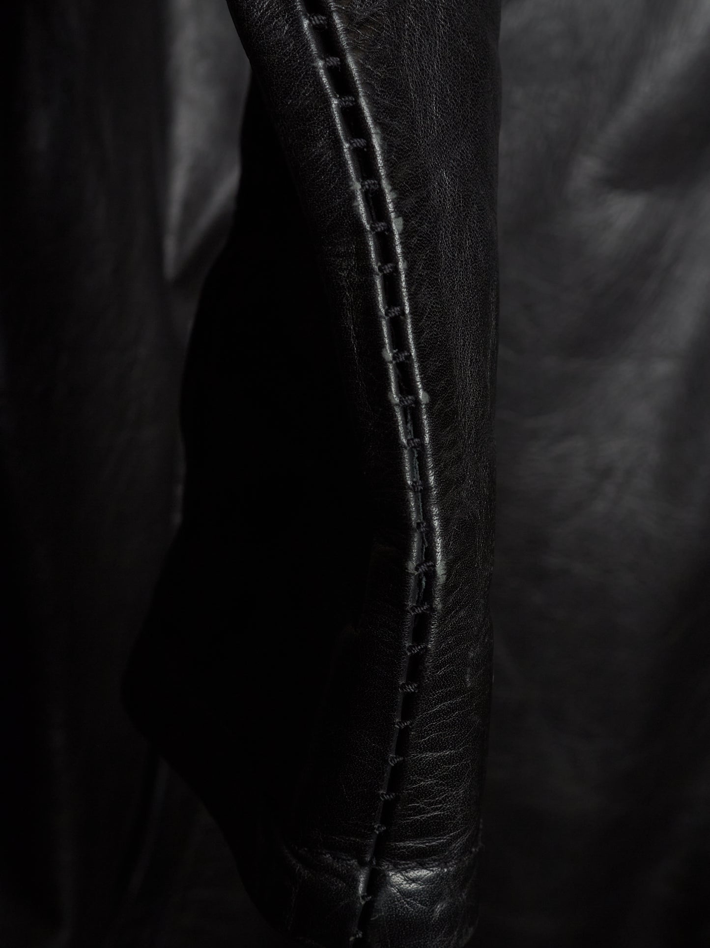 Close-up of a black leather garment, showing a seam with double stitching on a dark background.
