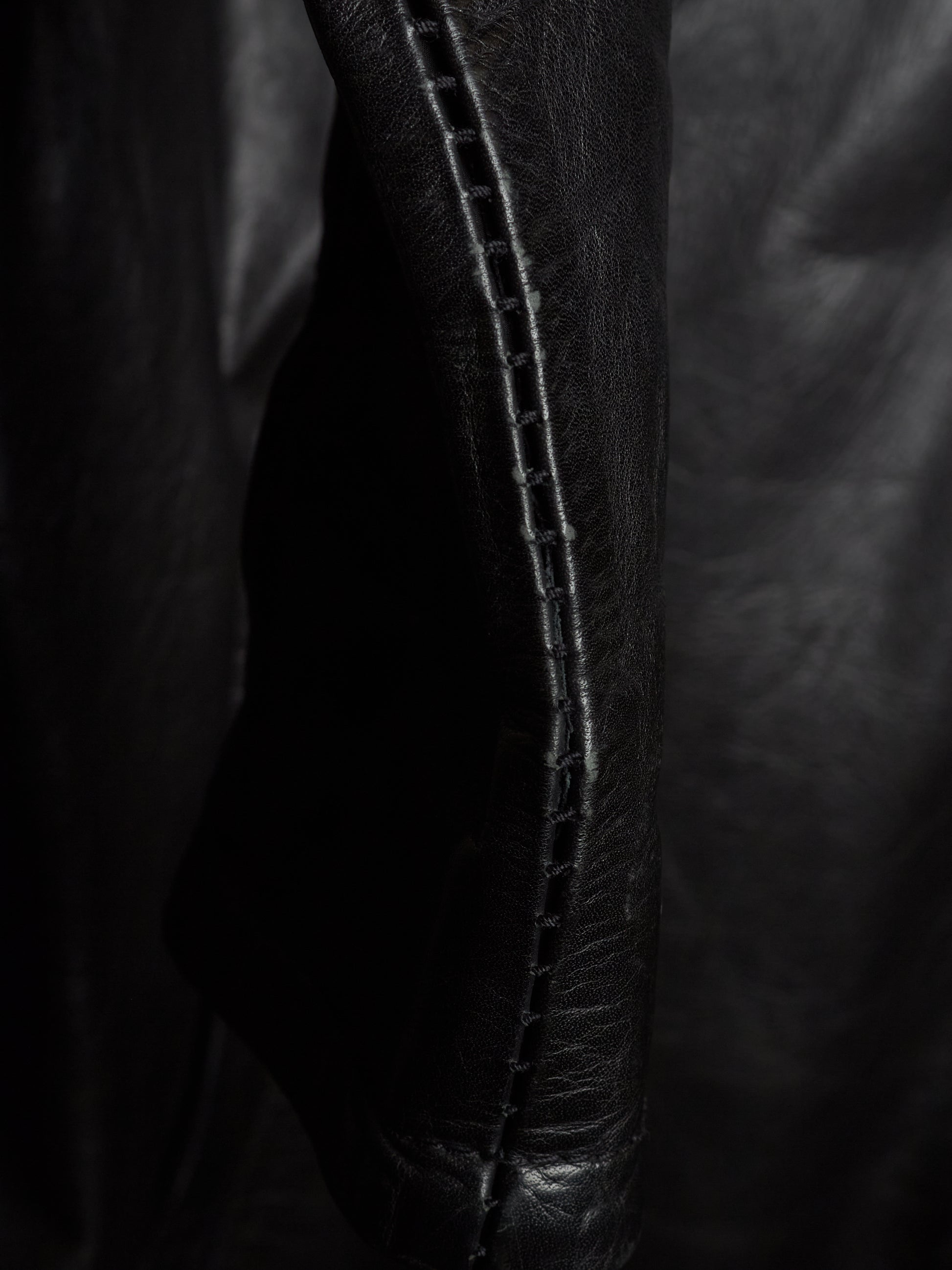 Close-up of a black leather garment, showing a seam with double stitching on a dark background.