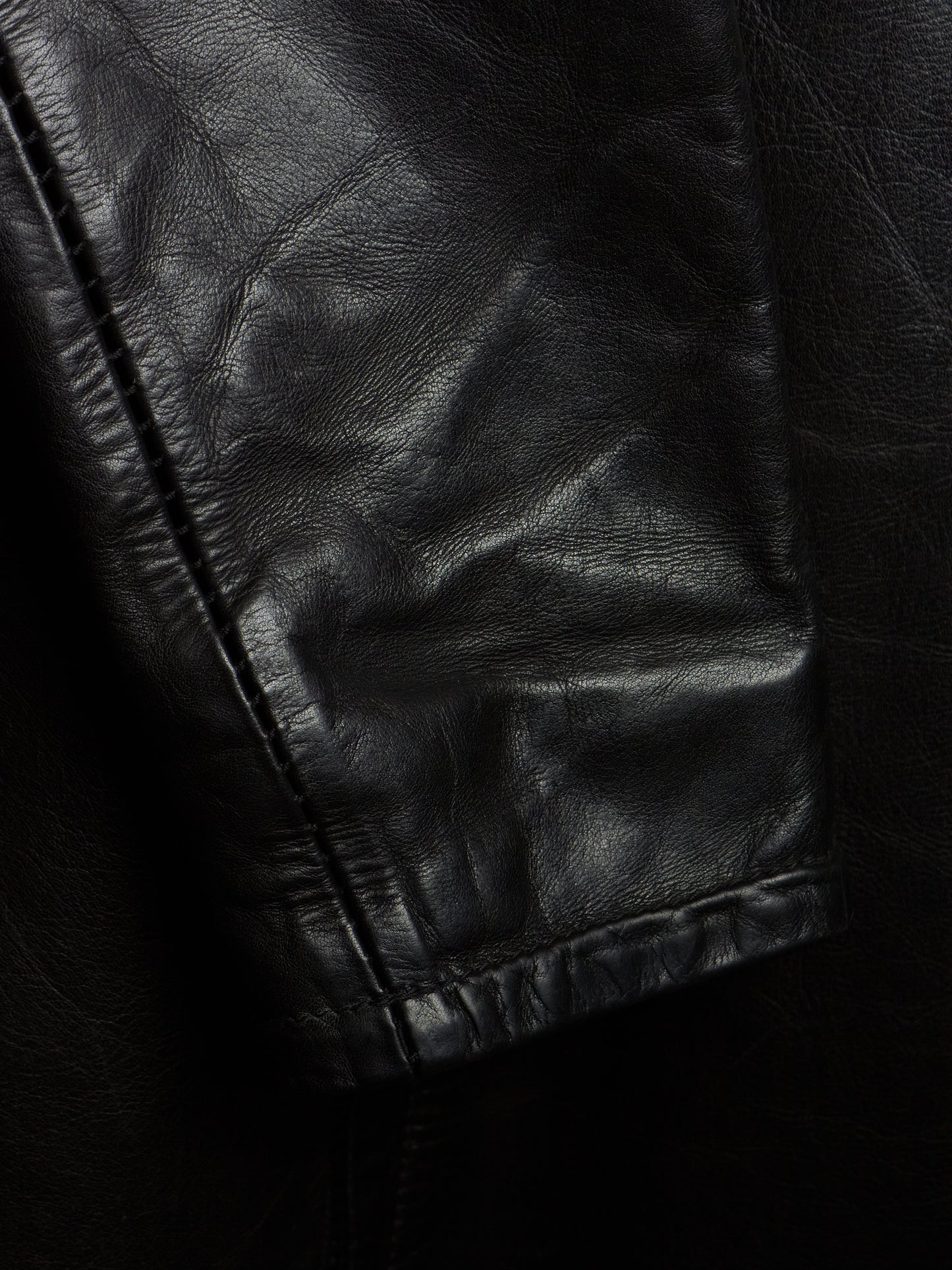 Close-up of a black leather jacket showing the texture and stitching of the sleeve cuff.