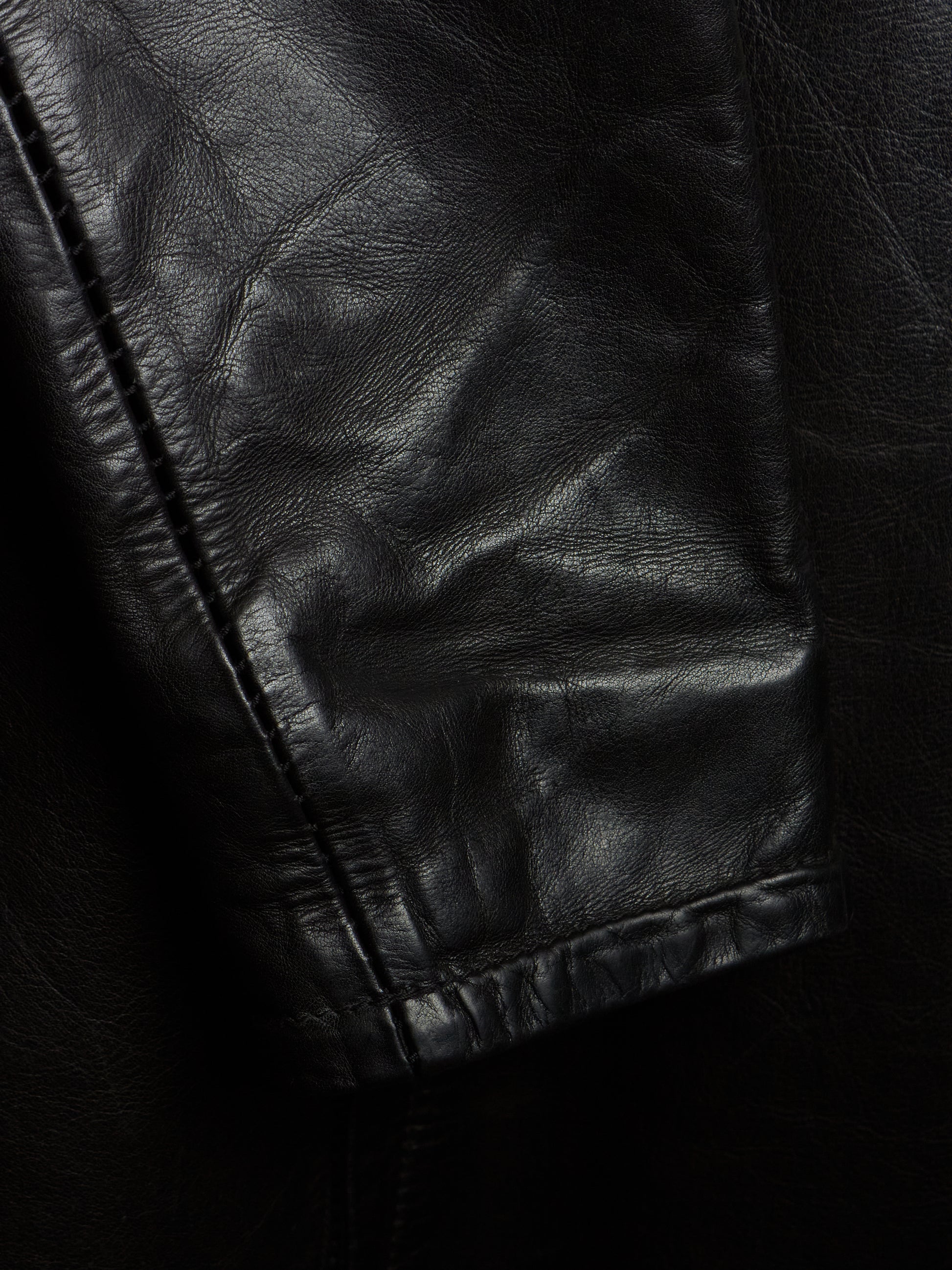 Close-up of a black leather jacket showing the texture and stitching of the sleeve cuff.