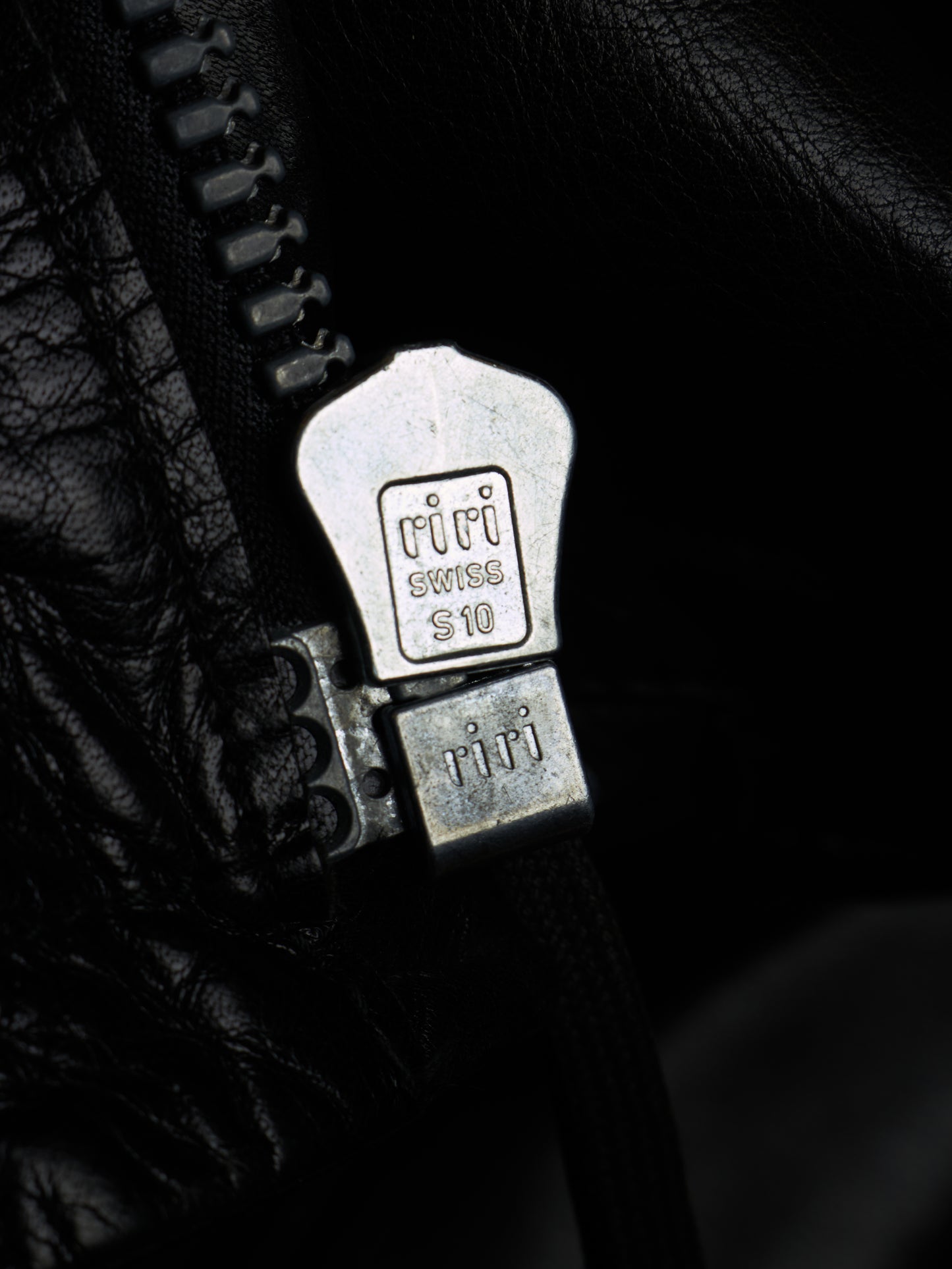 Close-up of a black leather zipper with a silver metal pull tab engraved with 'Tifi' and 'Swiss 10'.