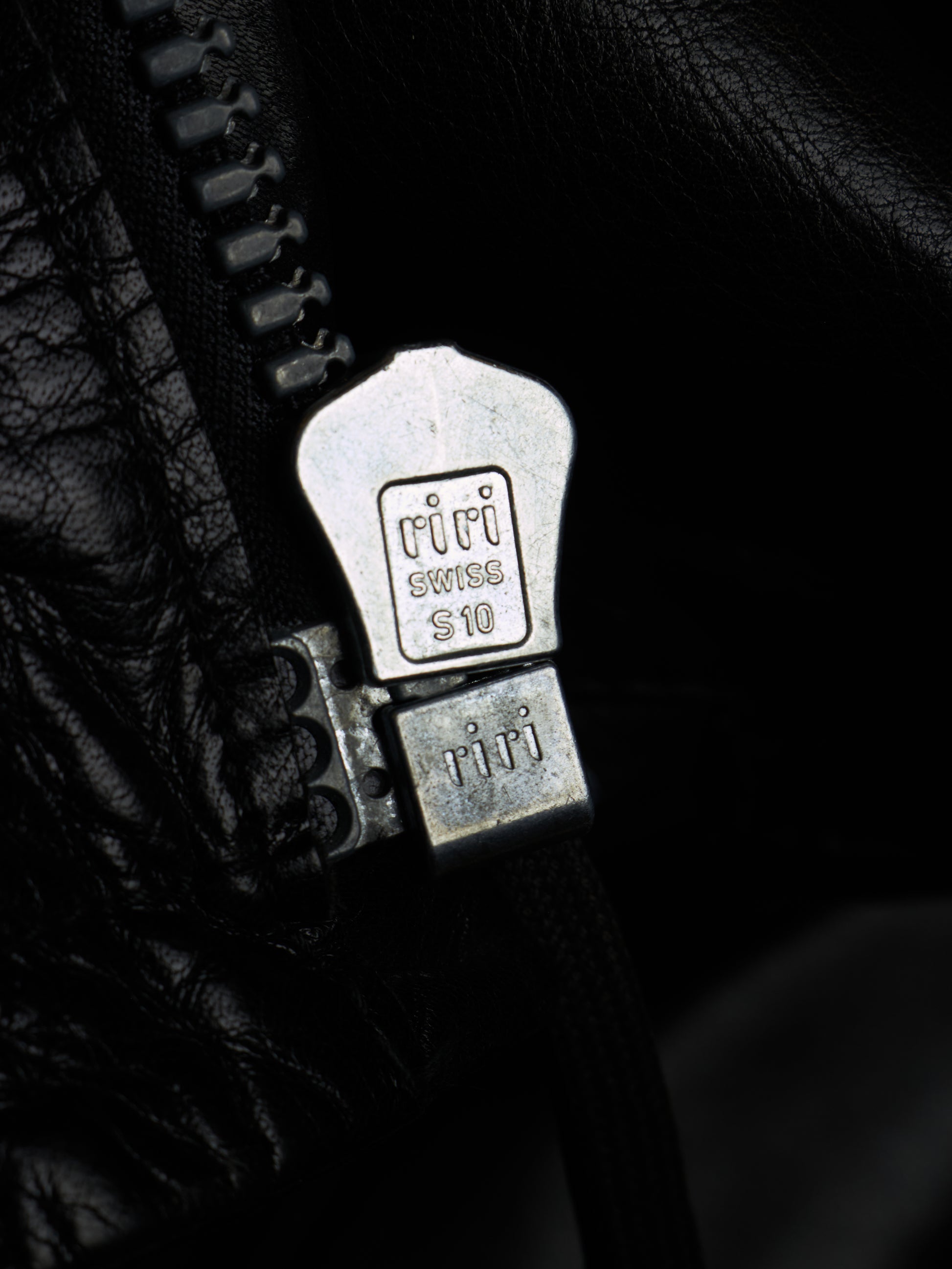 Close-up of a black leather zipper with a silver metal pull tab engraved with 'Tifi' and 'Swiss 10'.