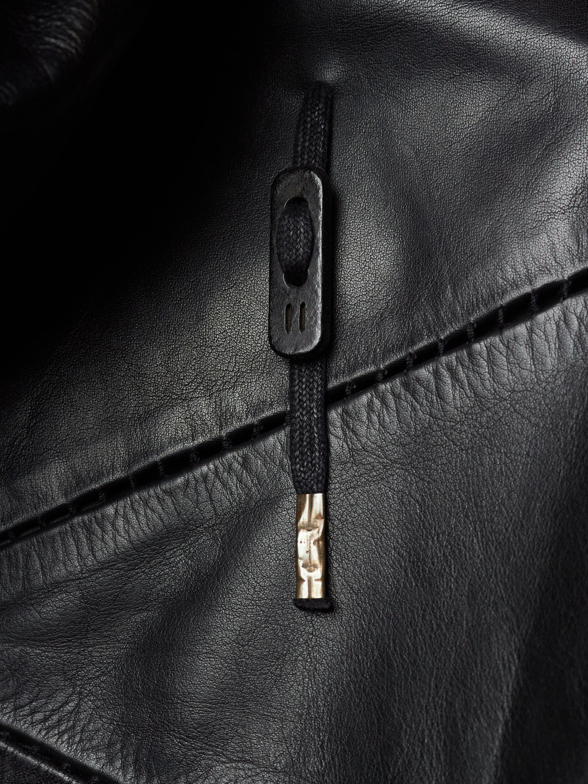 Close-up of a black leather jacket featuring a black zipper with a rectangular pull tab and a small gold-toned accent.