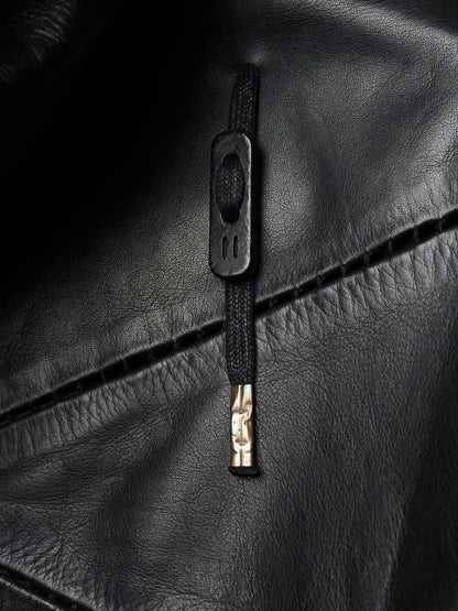 Close-up of a black leather jacket featuring a black zipper with a rectangular pull tab and a small gold-toned accent.
