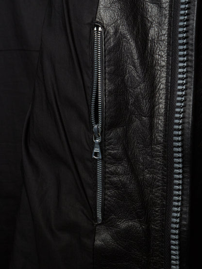 Close-up detail of a black jacket showing a vertical zippered pocket with matte black fabric on one side and textured black leather on the other, with a silver zipper pull.