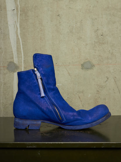 A single blue leather ankle boot with a side zipper, resting on a dark surface against a textured concrete wall.