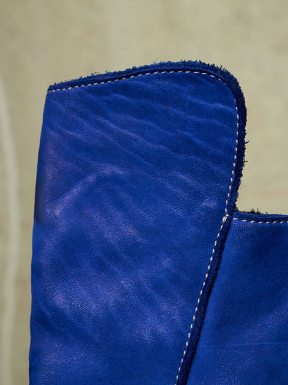 A close-up of a vibrant royal blue leather item, showing the texture of the leather and white contrast stitching against a neutral beige background.