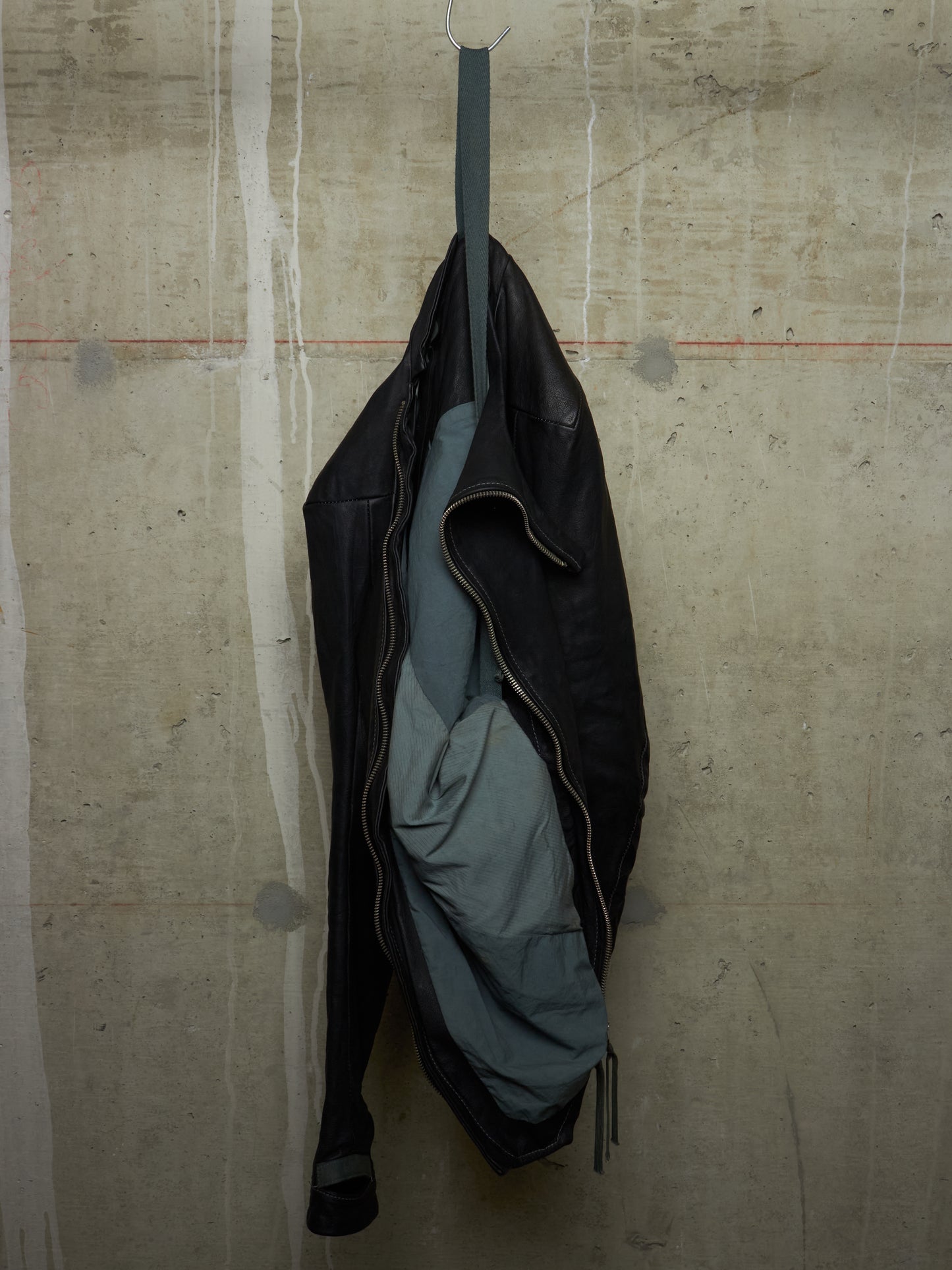 Black jacket with a gray lining hanging on a hook against a textured beige wall.