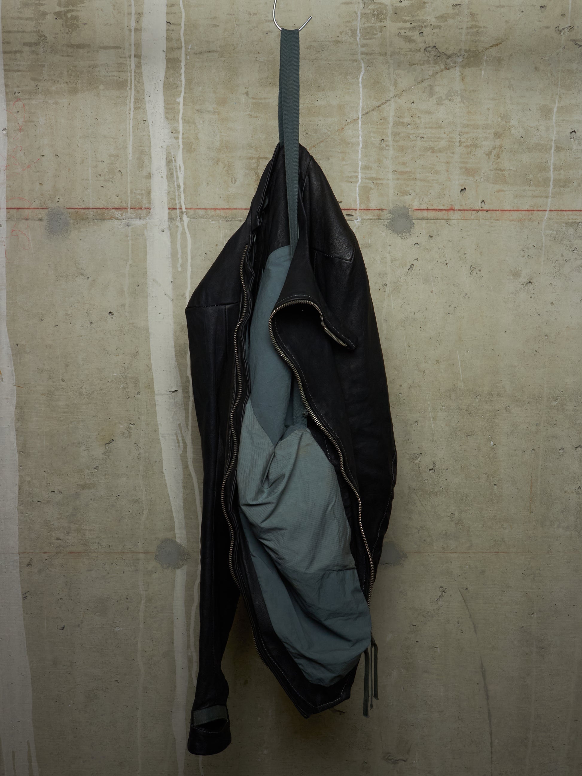 Black jacket with a gray lining hanging on a hook against a textured beige wall.