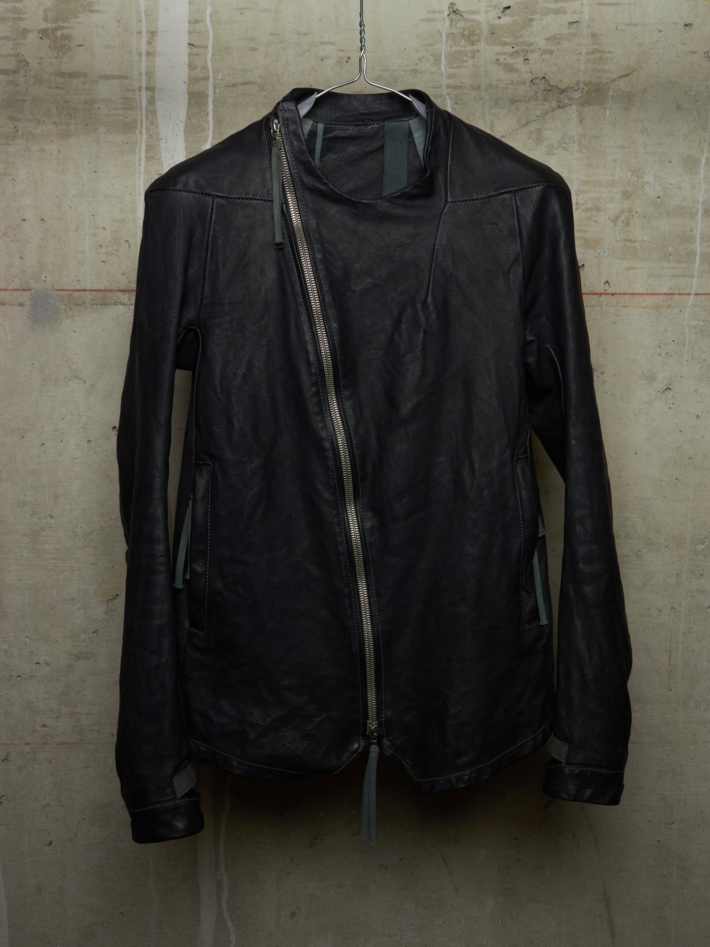 Black leather jacket hanging against a textured beige wall.