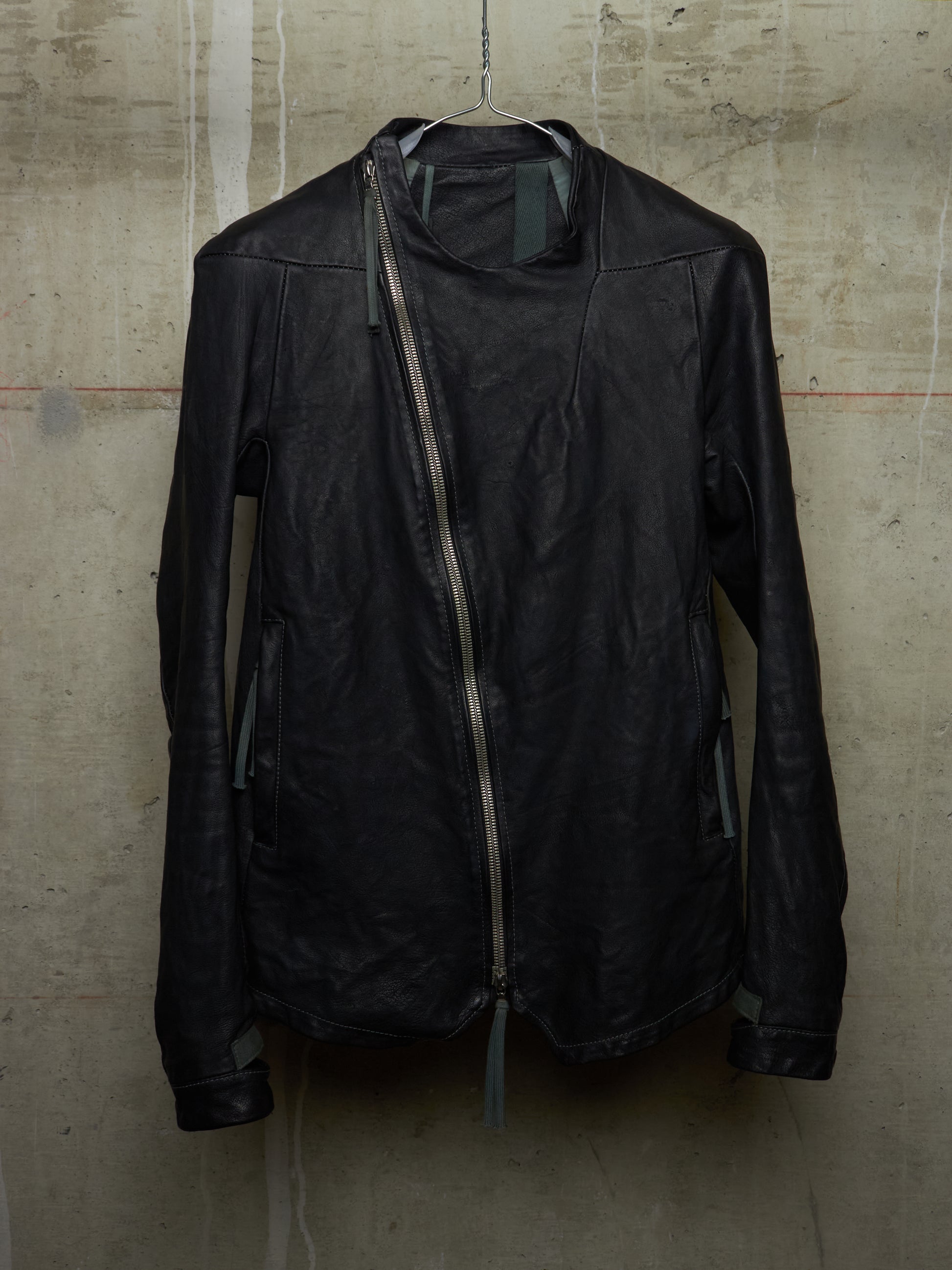 Black leather jacket hanging against a textured beige wall.