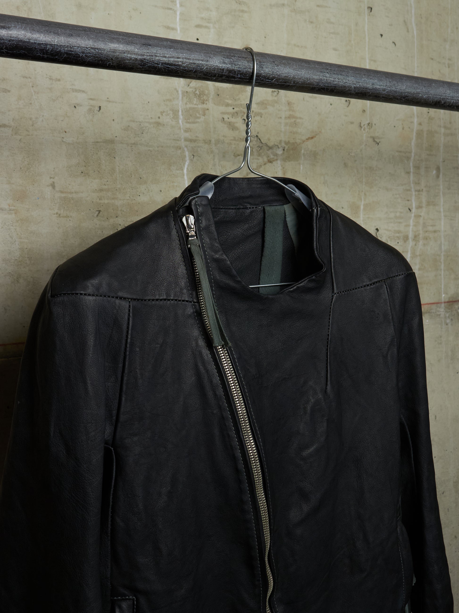 Black jacket hanging on a metal rod against a textured wall.