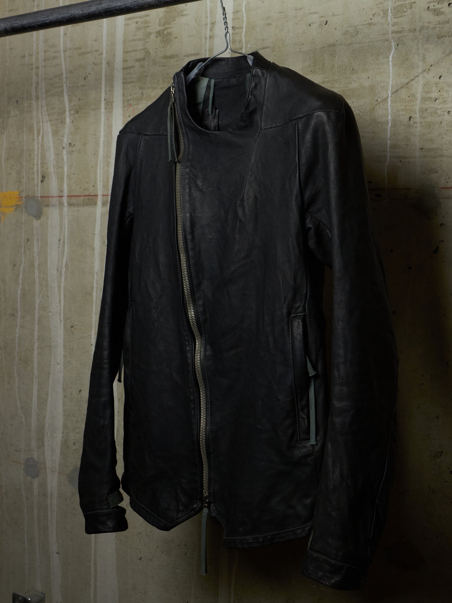 Black jacket hanging on a hanger against a textured wall.