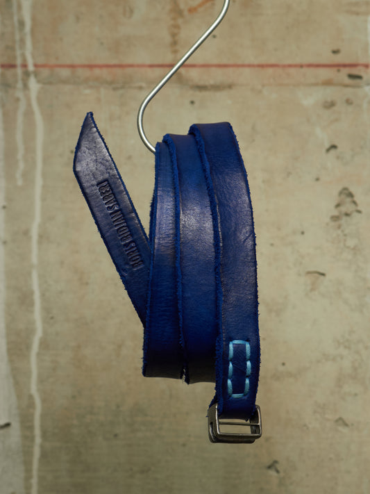 A dark blue leather belt with light blue contrast stitching and a silver metal buckle, hanging from a metal hook against a textured beige background.