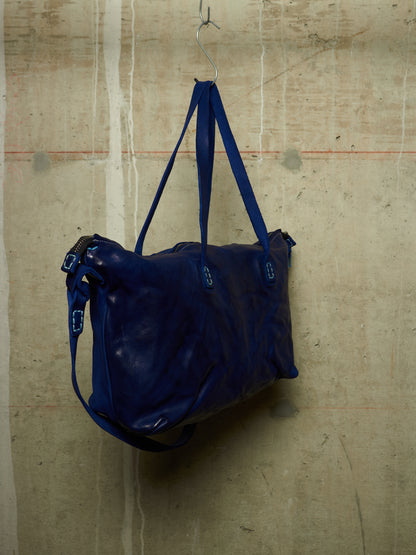 A dark blue leather duffel bag hanging from a metal hook against a textured concrete wall.