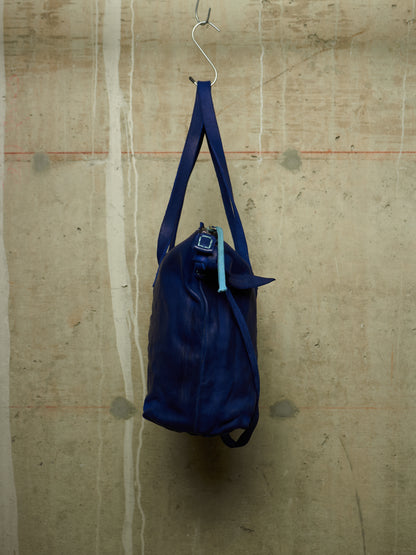 A dark blue leather duffel bag hanging from a metal hook against a textured concrete wall.