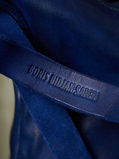 Close-up of a dark blue leather strap with the debossed brand name 'BORIS BIDJAN SABERI' on a textured blue fabric background.
