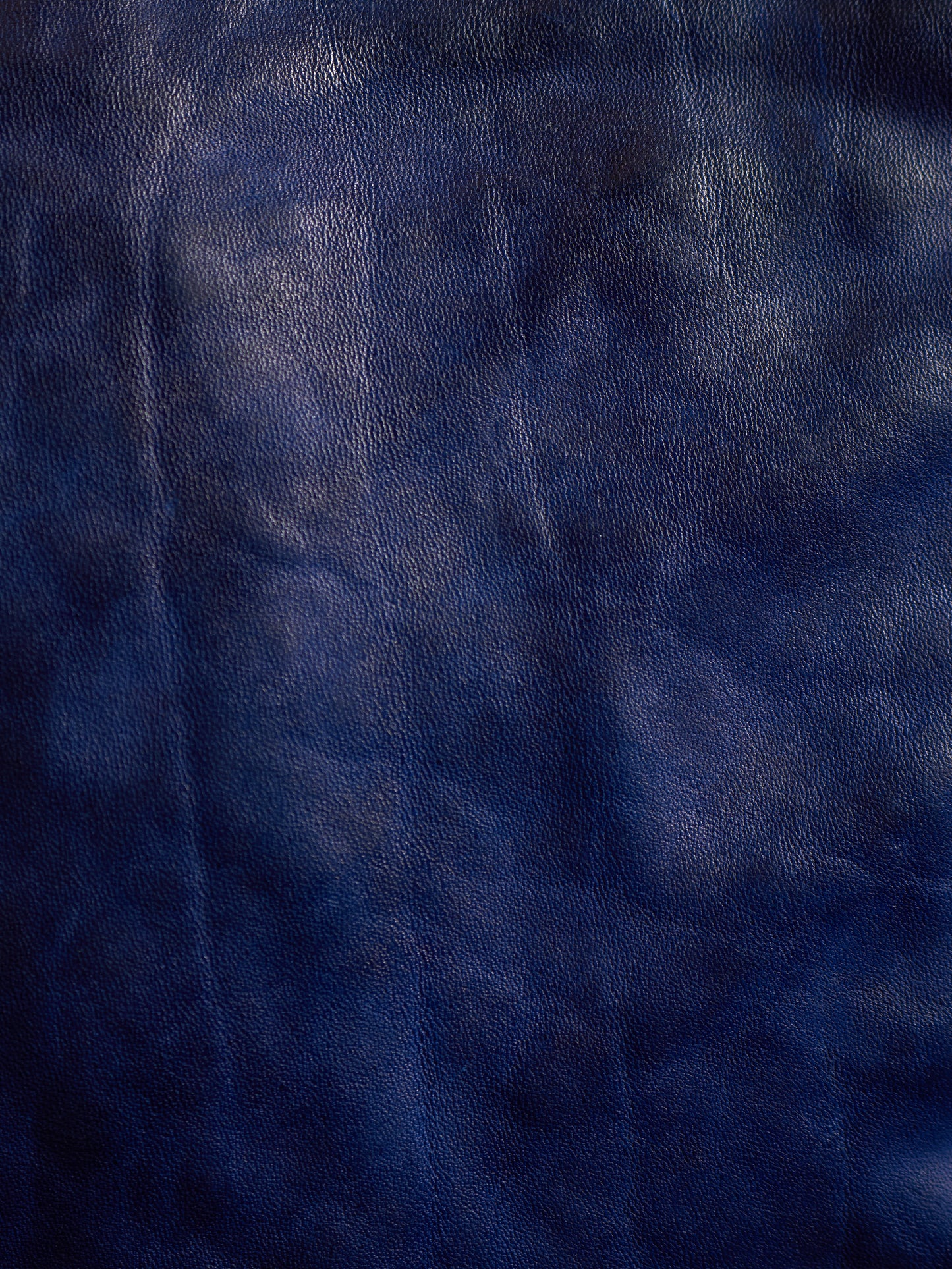 A close-up of dark navy blue textured material, resembling leather or faux leather with subtle sheen and grain.