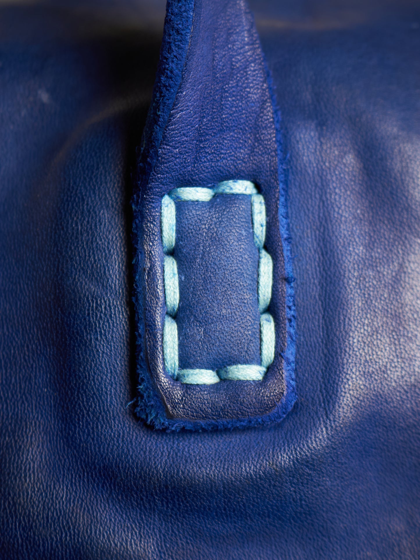 Close-up of a dark blue leather bag featuring a rectangular patch with decorative light blue contrast stitching.