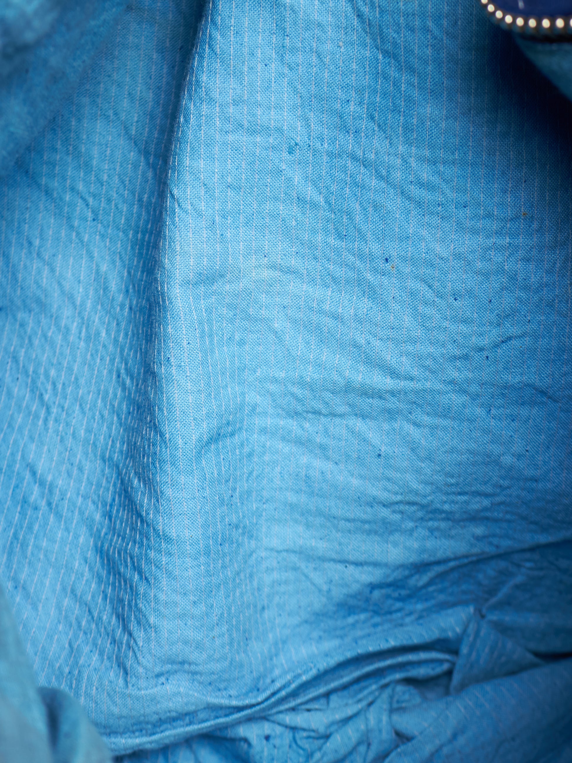 A close-up of crinkled blue fabric with a subtle vertical textured pattern.