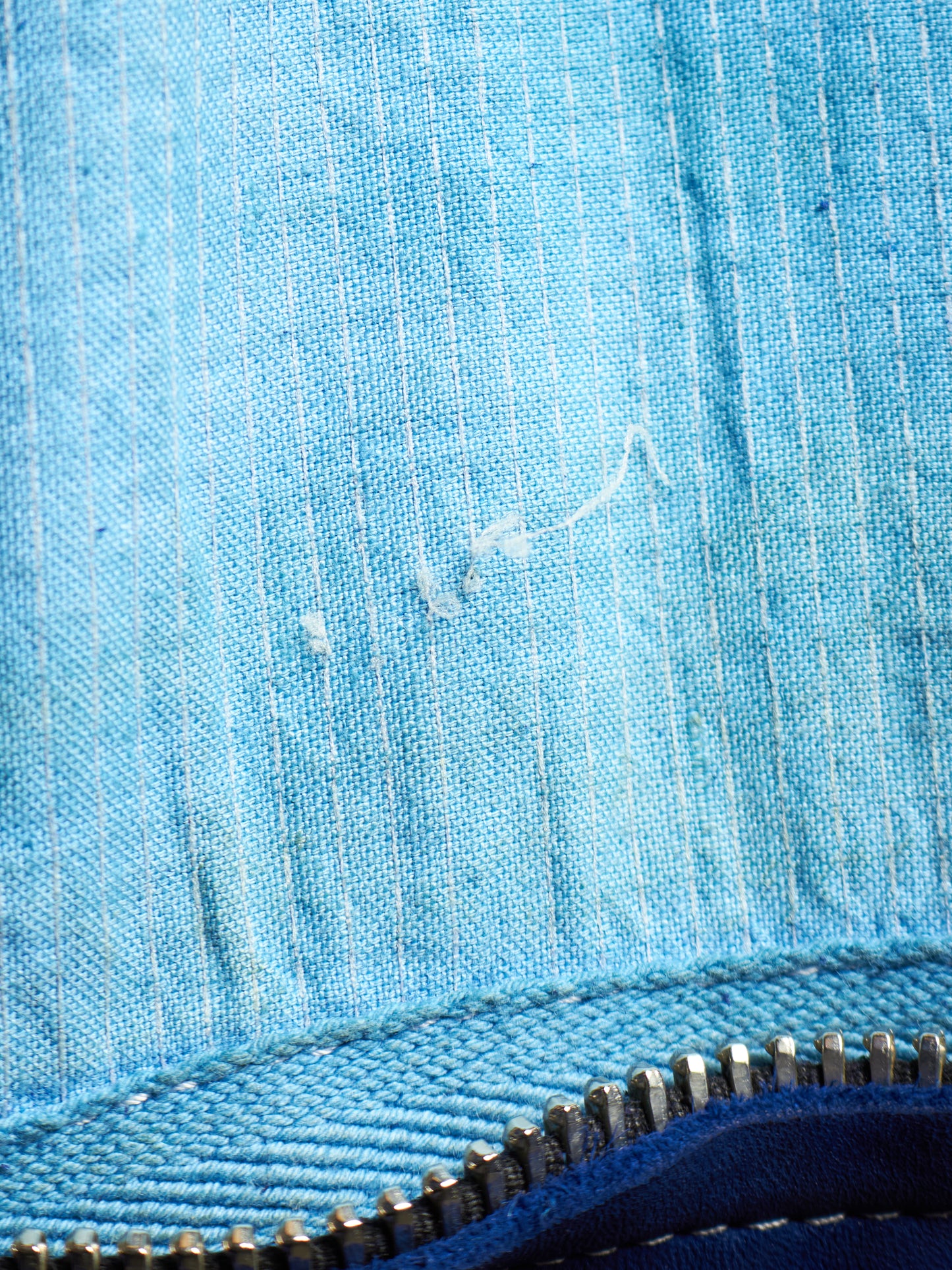 Close-up of a light blue textured fabric surface with a white scratch or mark, plus a blue zipper running along the bottom edge.