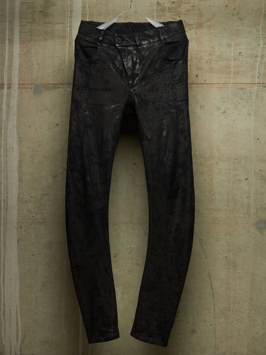 Black distressed leather pants hanging on a white hanger against a textured concrete wall.