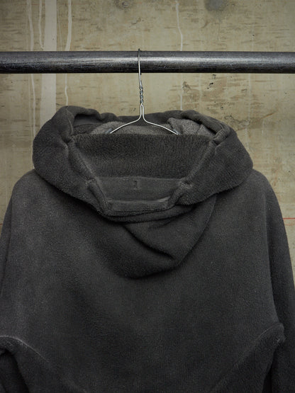 A dark charcoal gray hooded sweatshirt hanging from a metal hanger on a horizontal rod against a textured concrete wall.
