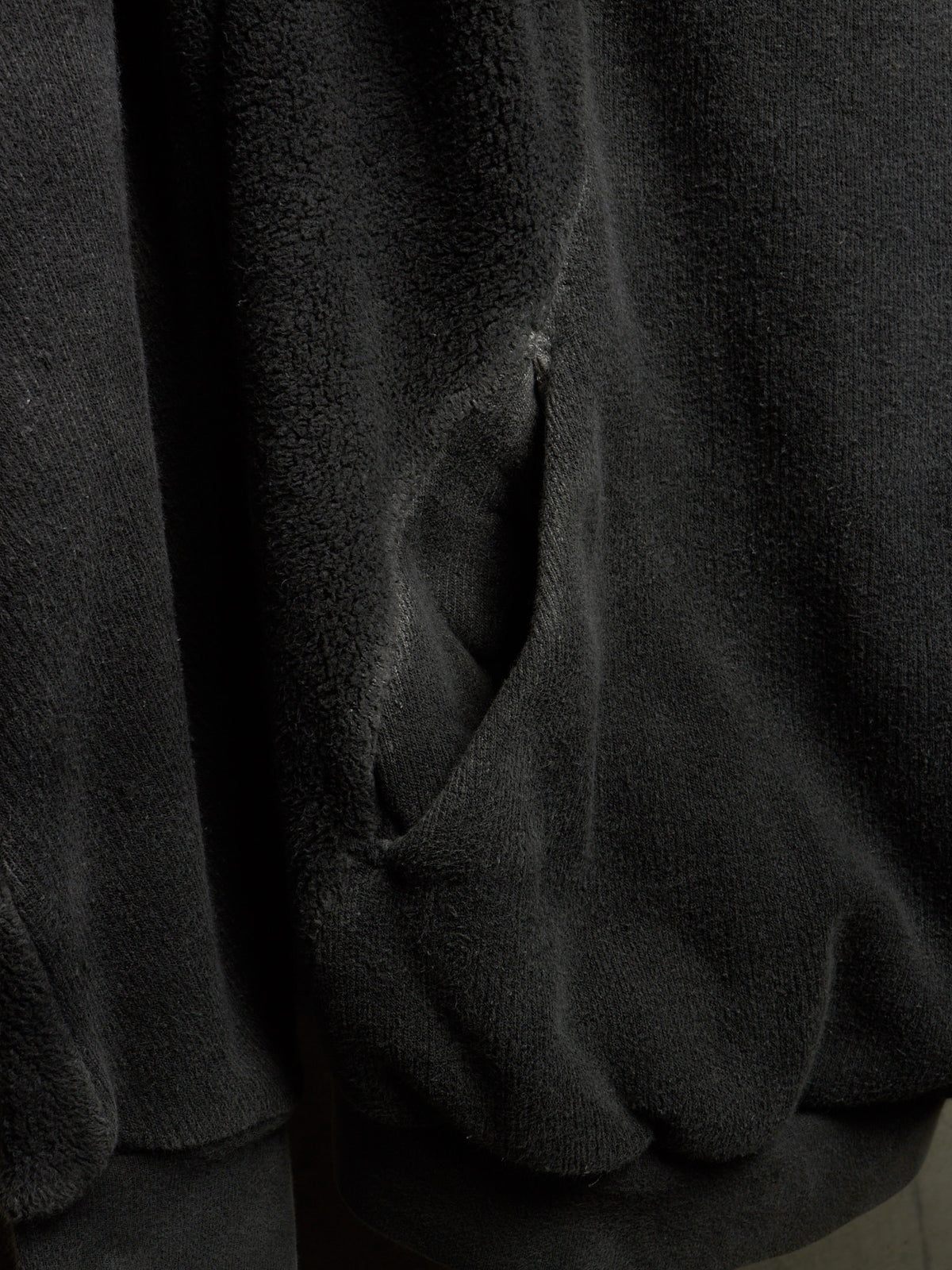 Close-up of a dark charcoal gray plush fleece fabric with a visible stitched pocket opening.