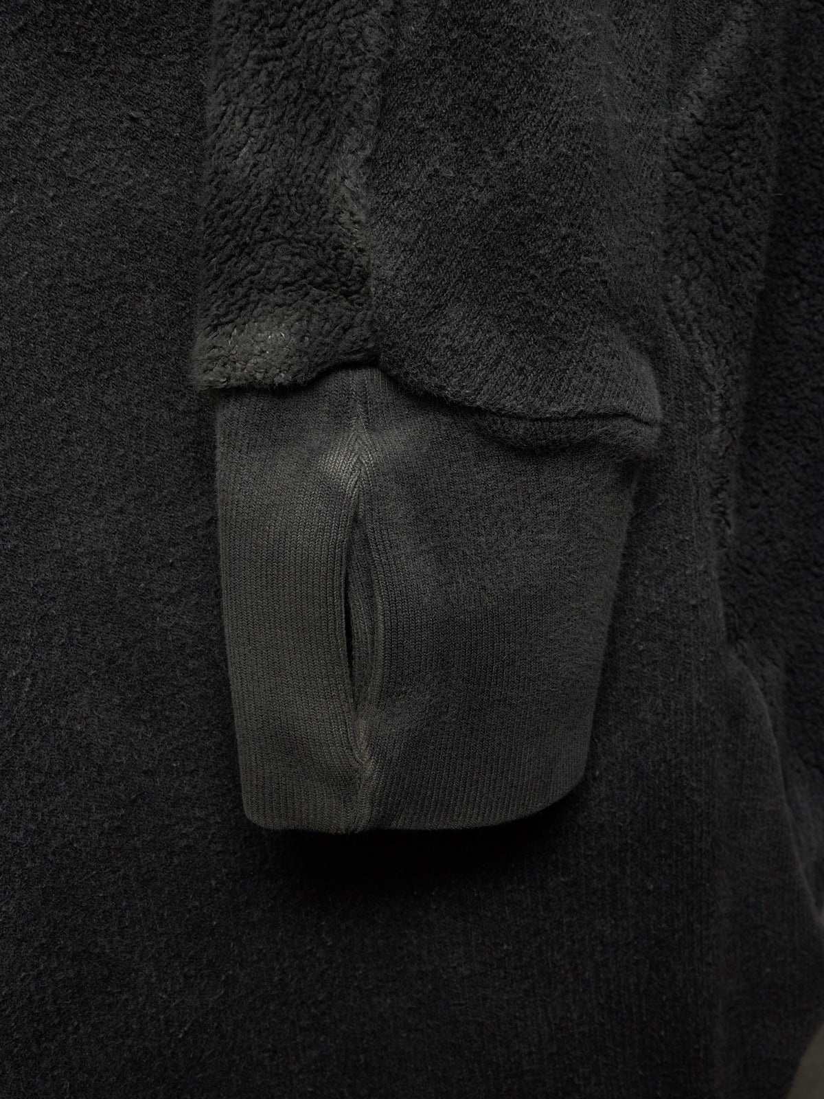 Close-up detail of a dark charcoal gray fleece or sherpa garment with a ribbed knit cuff and a small slit opening.