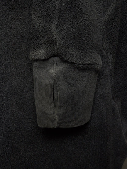Close-up detail of a dark charcoal gray fleece or sherpa garment with a ribbed knit cuff and a small slit opening.