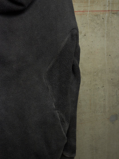 Close-up of a dark charcoal gray fleece or terry cloth garment, showing the fabric texture and a seam, set against a concrete wall background.