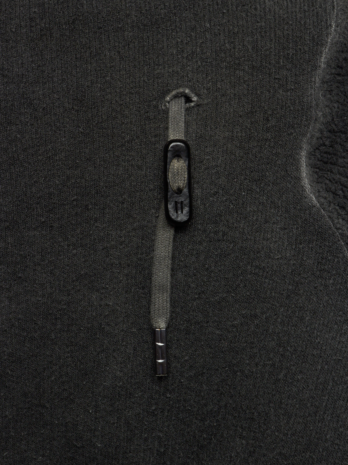Close-up of a dark charcoal gray knit fabric with a vertical zipper and a small black pull tab.