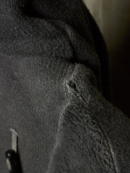 Close-up of a dark gray textured fleece or sherpa fabric surface with a small dark button or toggle visible at the lower left.