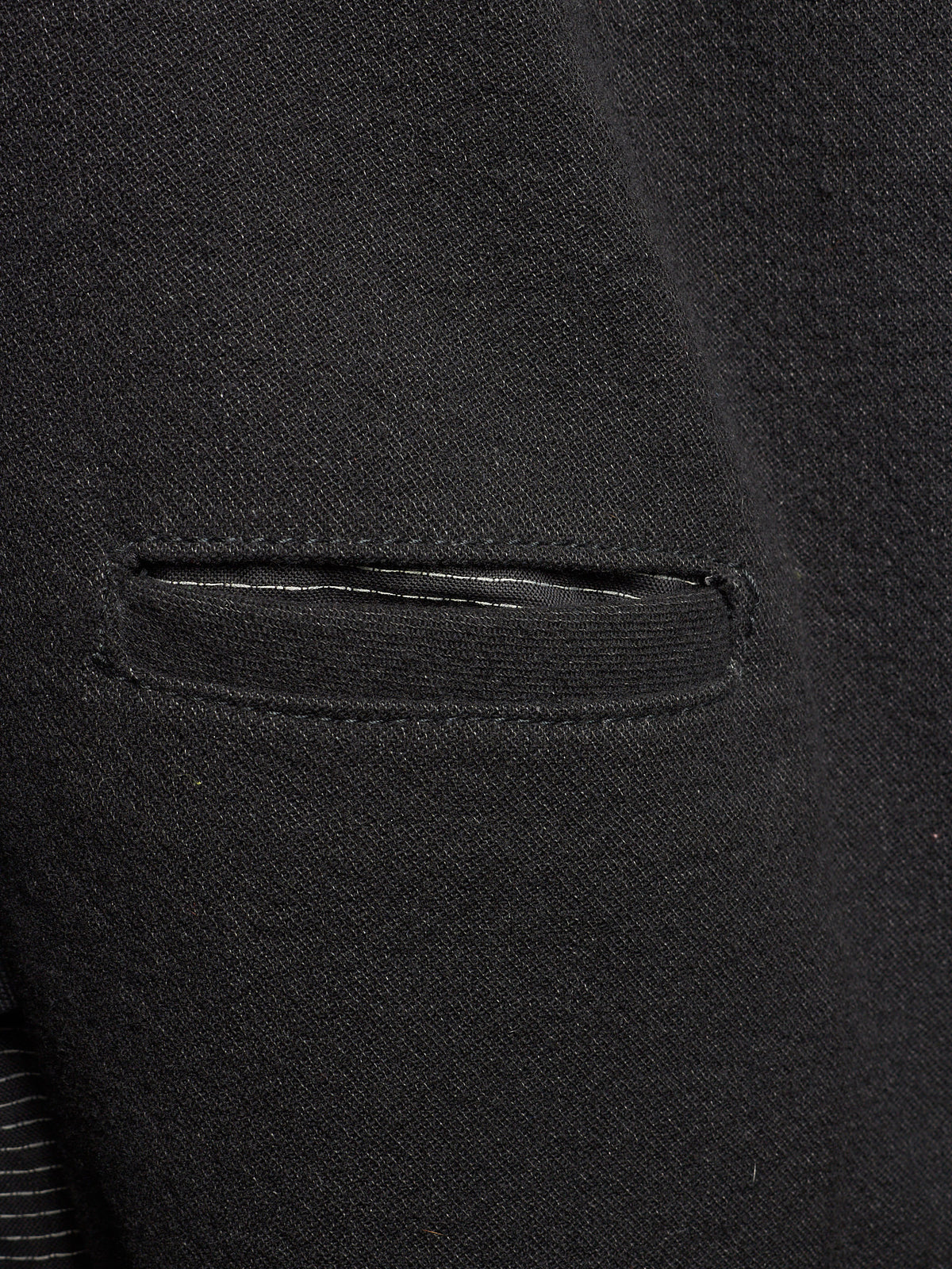 Close-up of a black textured fabric garment showing a horizontal welt pocket and fine knit or woven texture.