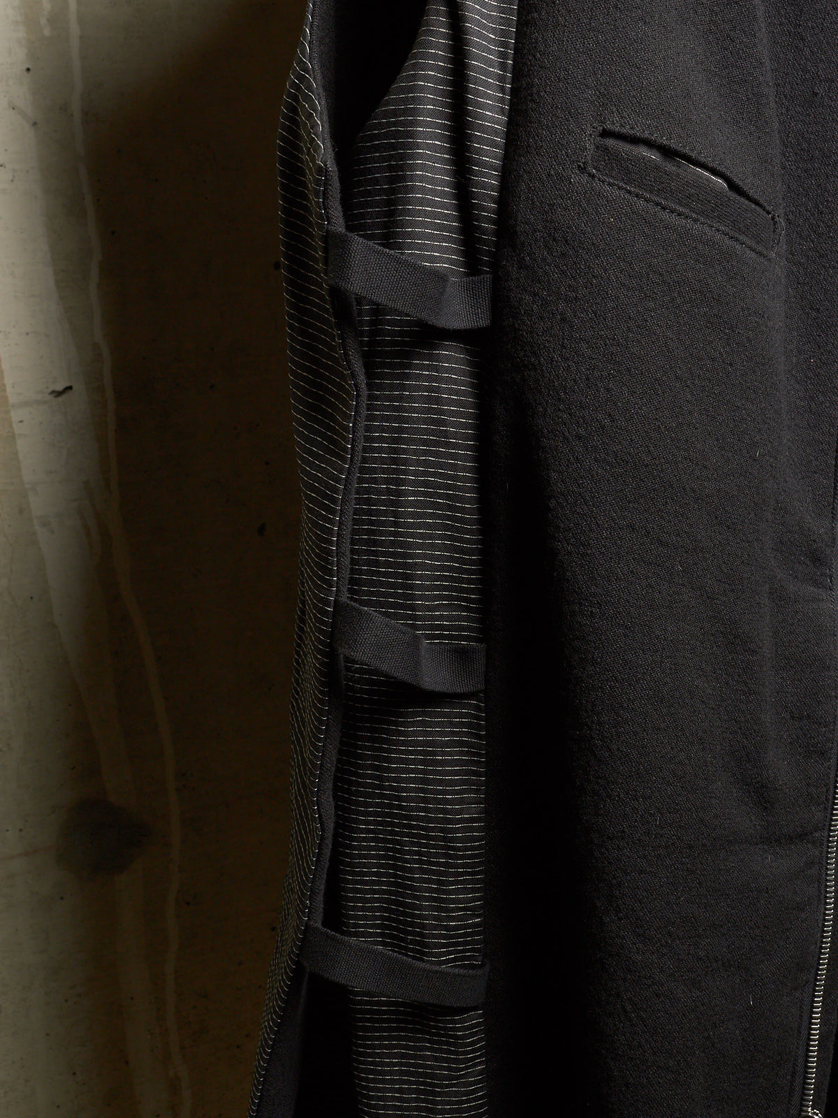 Close-up of a dark charcoal gray coat with a textured, slightly fuzzy outer fabric, a fine striped lining, and a zippered pocket.