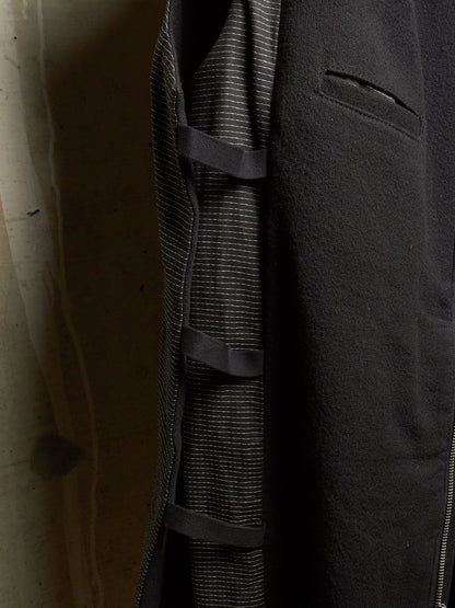 Close-up of a dark charcoal gray coat with a textured, slightly fuzzy outer fabric, a fine striped lining, and a zippered pocket.