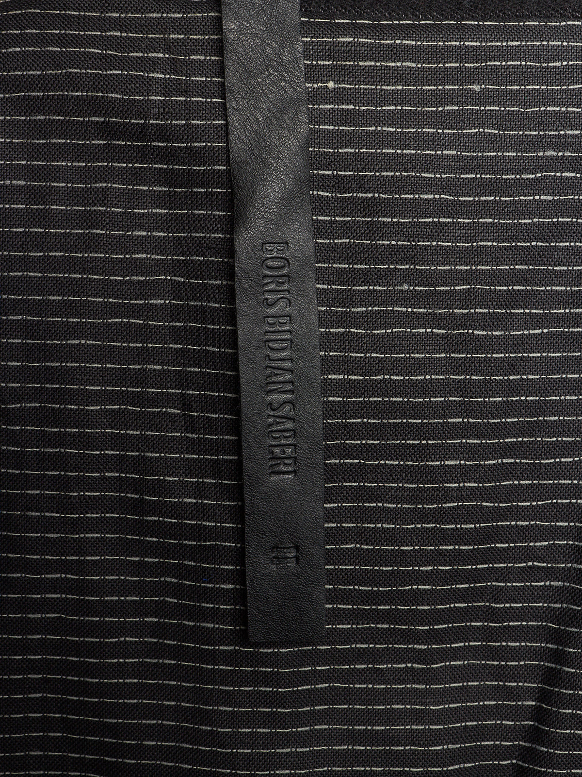 Close-up of a black and white striped knit fabric with a vertical black leather brand tab reading EONS BIDANS AHER.