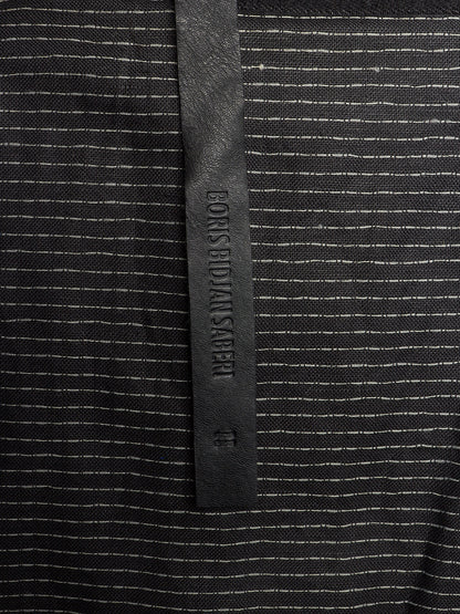 Close-up of a black and white striped knit fabric with a vertical black leather brand tab reading EONS BIDANS AHER.