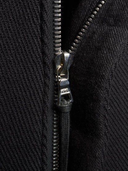 Close-up of a black textured zippered garment with a silver metal zipper pull and black cord lock.