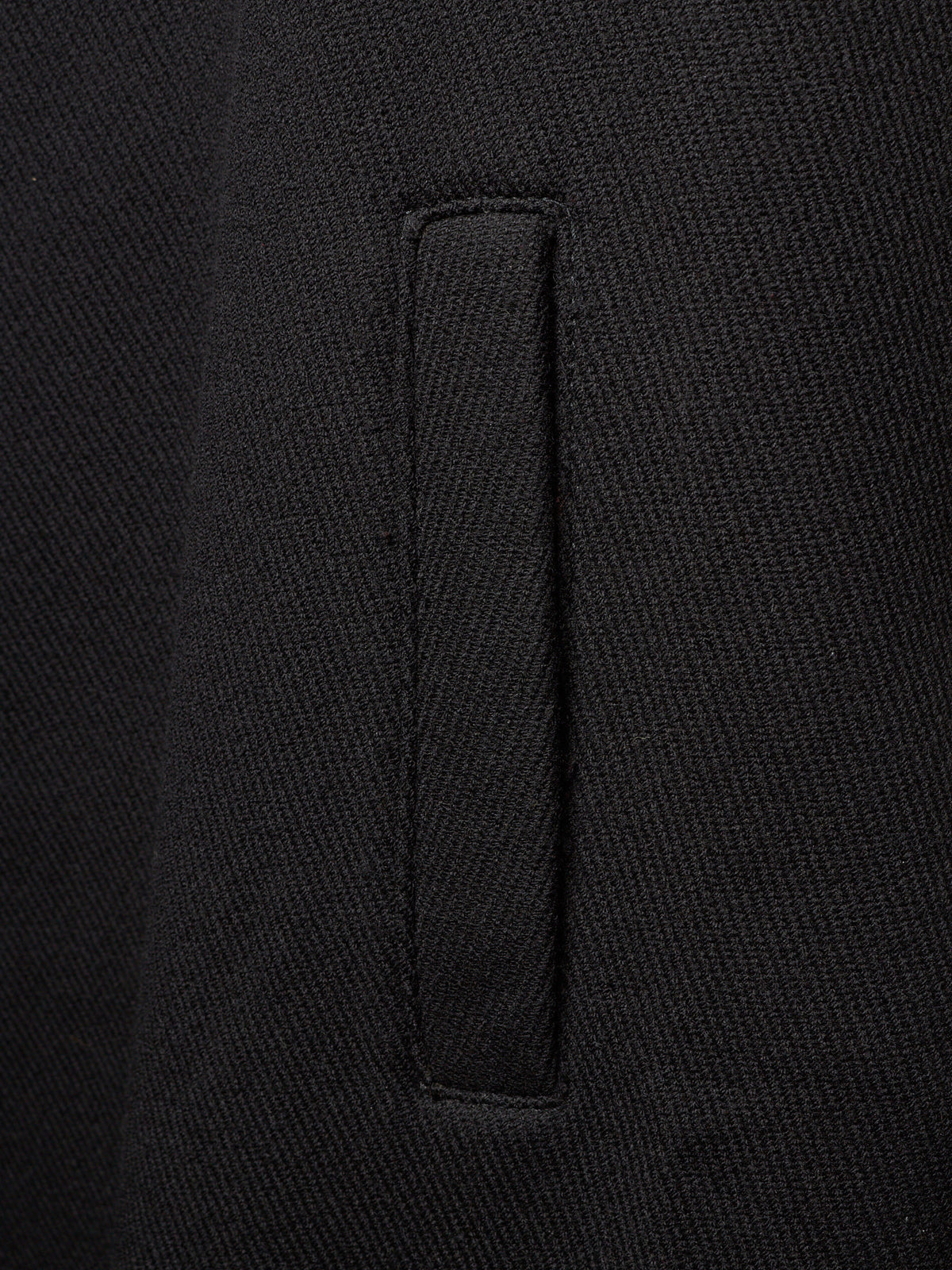 Close-up of a black woven fabric garment showing a vertical welt pocket detail.