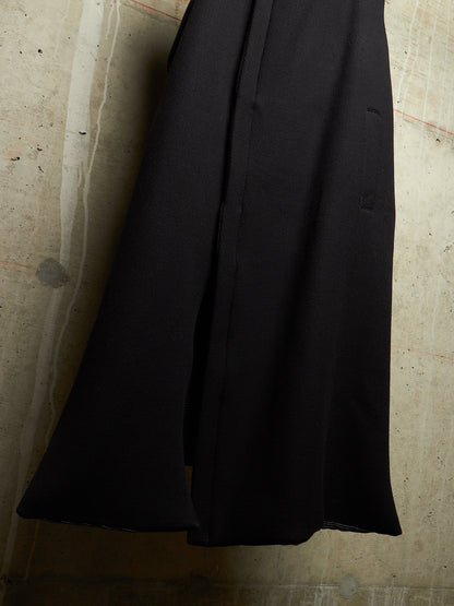 A close-up of a black wide-leg skirt or drape of fabric hanging against a textured concrete wall.