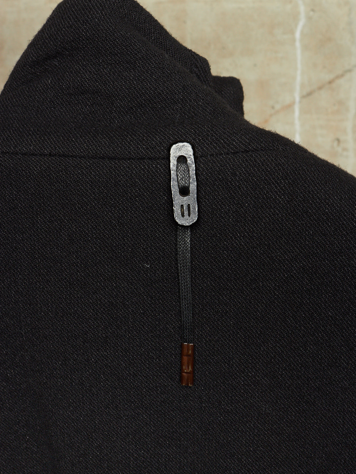 Close-up of a black textured garment featuring a decorative silver metal zipper pull with a dark cord and a small brown wooden accent at the bottom.